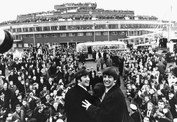 The Beatles on the steps of a plane, with adoring fans in front of them