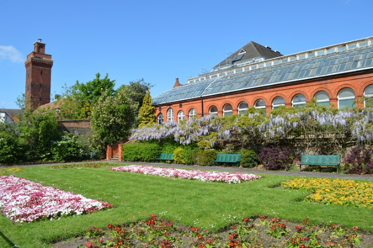 Best London gardens to visit: a long, redbrick building with a glass roof, behind a park with a tidy lawn and colourful flowerbeds