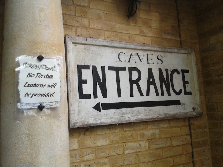Best things to do in outer London:  a wooden painted sign on a brick wall reading "CAVES ENTRANCE" with an arrow pointing left