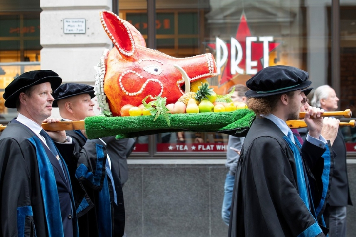 Four people in robes carrying a papier mache boar's head through the streets