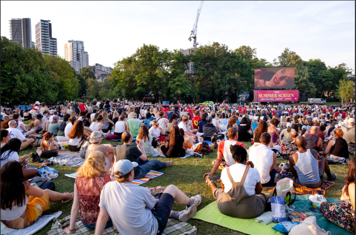 Outdoor cinema London summer 2026: people sitting on grass watching a large screen in Vauxhall