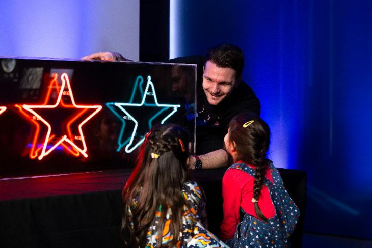 Top events in London this weekend: a man showing two girls a display with neon stars