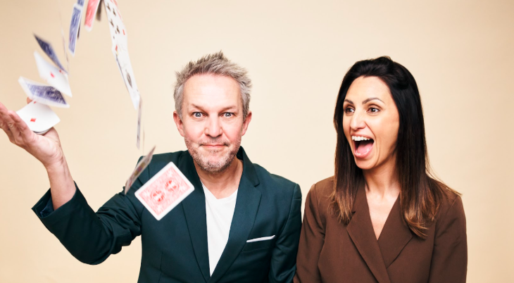 Things to do in London today: a man throwing a stack of playing cards into the air, with a woman sitting alongside him