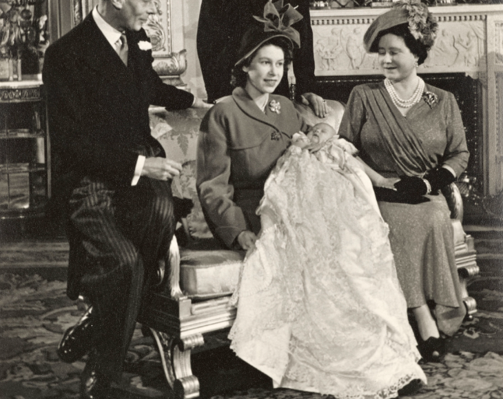 Top events in London today: a black and white photograph of Queen Elizabeth II and the Queen Mother sitting on a sofa, with a baby in a christening gown