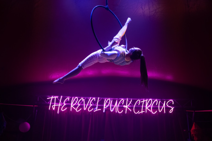 Top events in London today: an acrobat performing on a suspended hoop, above a neon pink "The Revel Puck Circus" sign