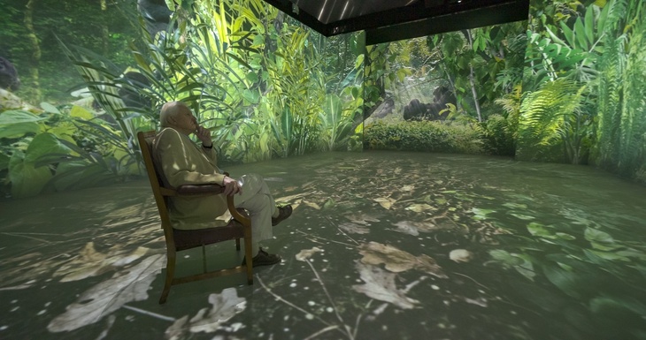 David Attenborough in a chair surrounded by screens showing the jungle