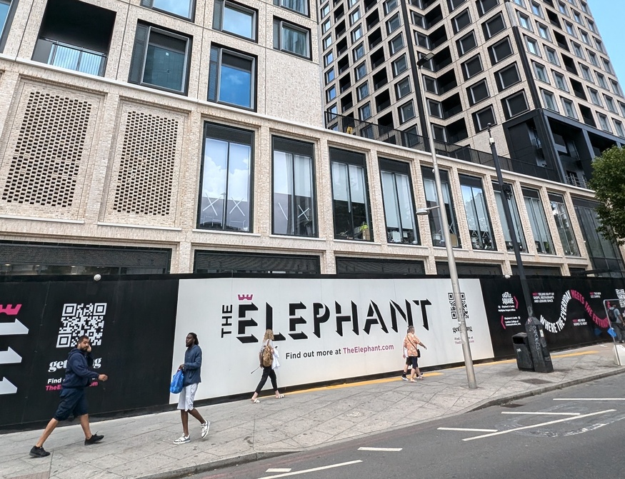 People walking past a big sign: The Elephant