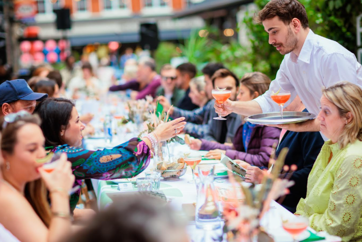 Top things to do in London in May 2026: a waiter serving drinks to people at a long table in the open-air