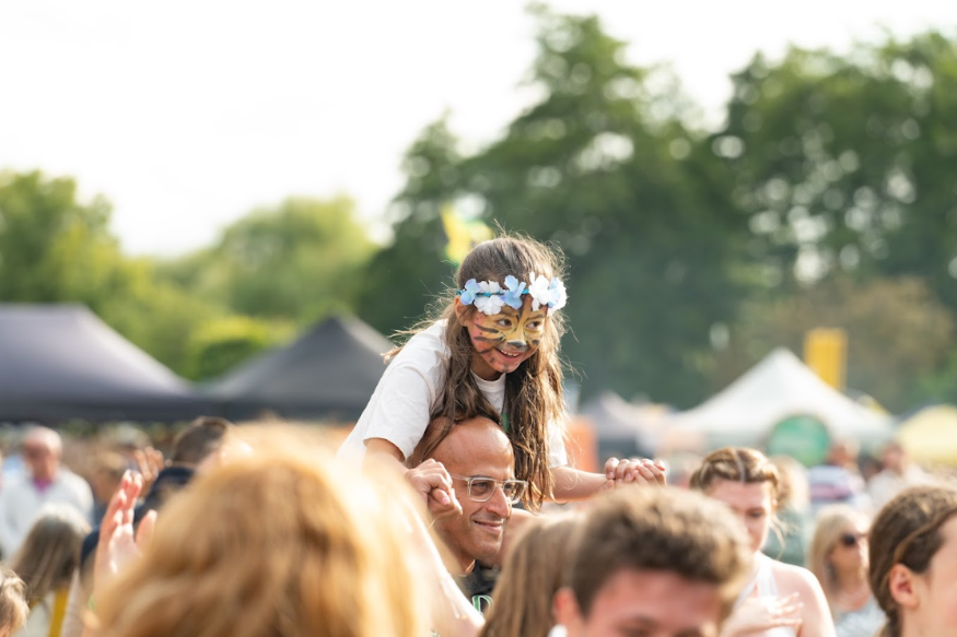 Things to do in London in May half term: a young girl with face painted like a tiger, sitting on a man's shoulders in a festival crowd