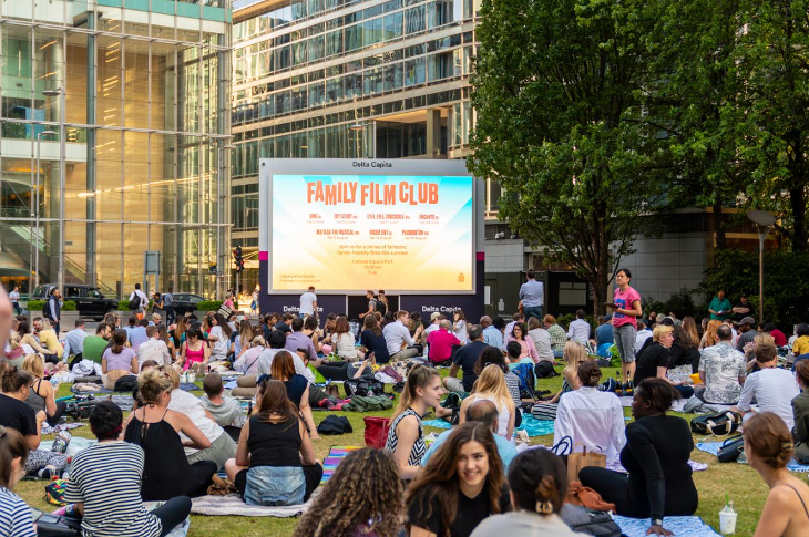 Outdoor film screenings in London: people sitting in groups on the grass in front of a large screen
