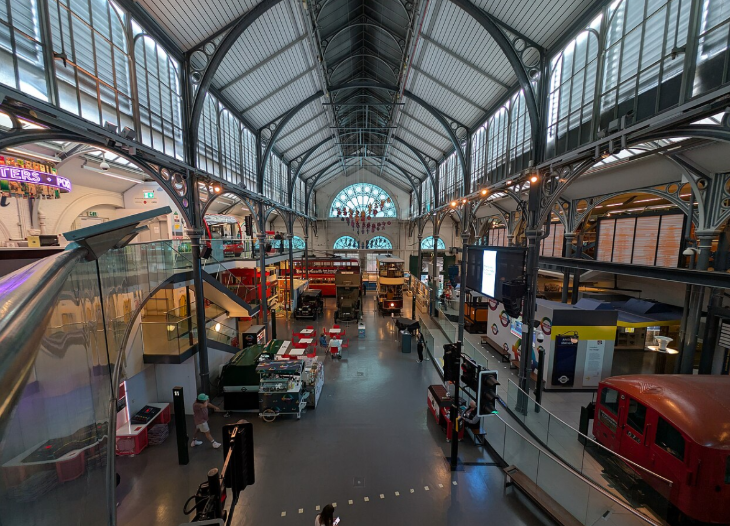 Things to do in London in May half term: High-angle view of the interior of the London Transport Museum, featuring a large hall with a vaulted glass and iron ceiling, filled with vintage buses, trams, and trains.