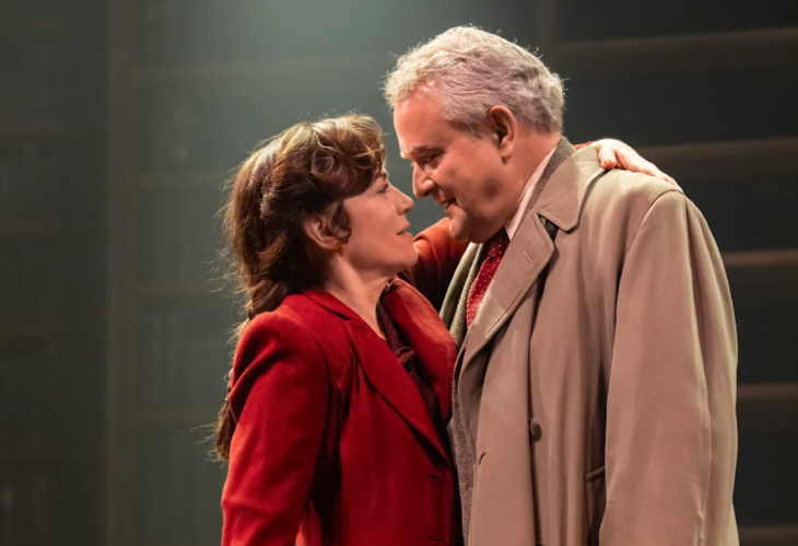 What's on in London this weekend: Maggie Siff in a red coat and Hugh Bonneville in a beige coat embracing on stage in Shadowlands