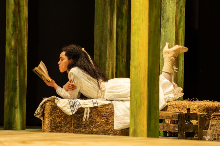 Things to do in London today: an actor on stage lying on her stomach on a bale of hay reading a book