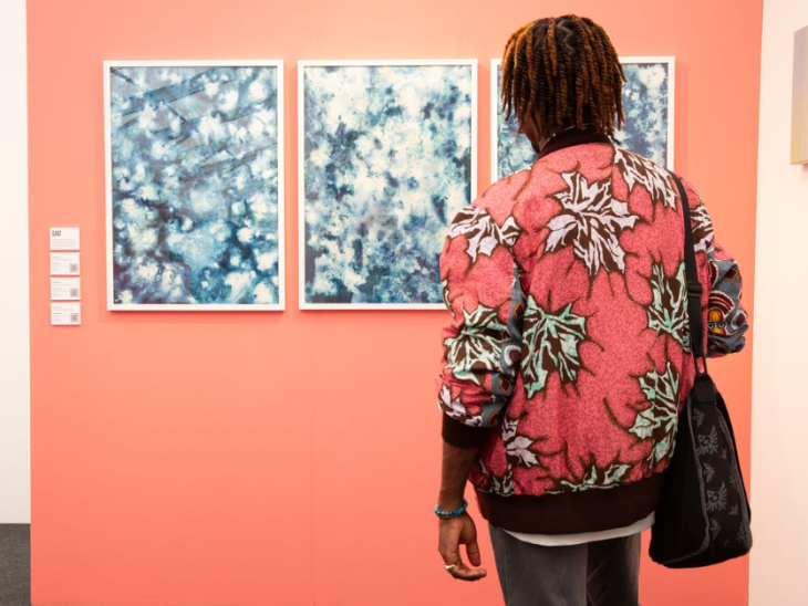 What's on in London this weekend: a person admiring a triptych painting mounted on a salmon-coloured wall