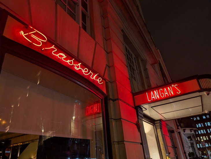 A low-angle night shot of Langan's Brasserie, featuring a glowing red neon 