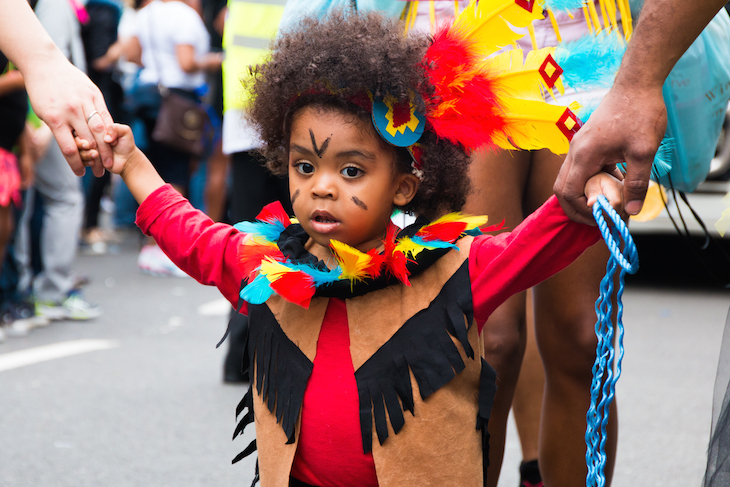 Notting Hill Carnival 2026: a young child in a costume and feathered headress at Notting Hill Carnival