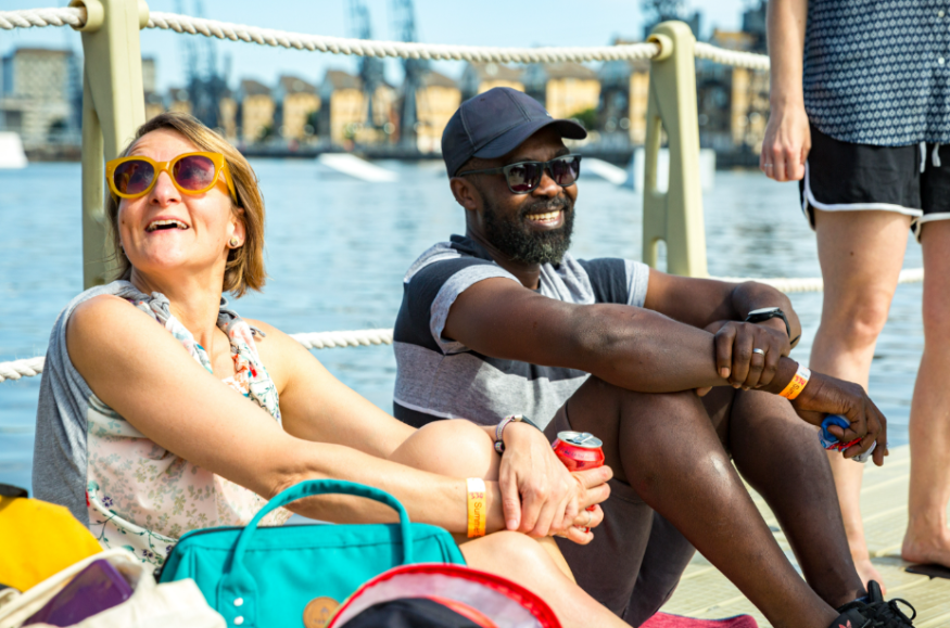 Beaches in London summer 2026: a man and woman with drinks in hand sitting by the water at Royal Docks