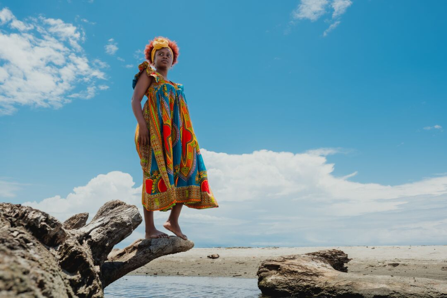 A photograph of a woman standing on a log at the beach
