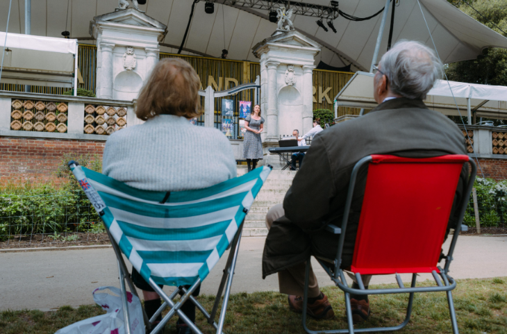 Two people sitting on camping chairs watching a performance on the steps in Holland Park