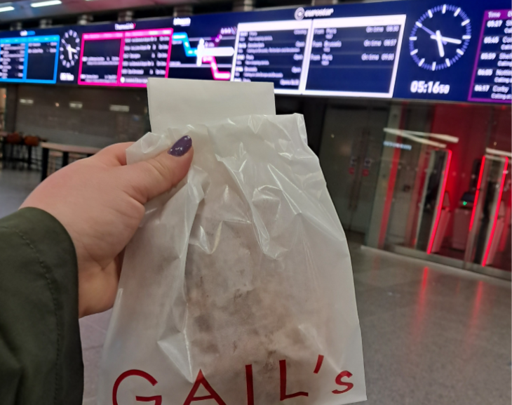 Extreme day trip from London to Lille: a hand holding a Gail's bakery bag up in front of Eurostar departure boards