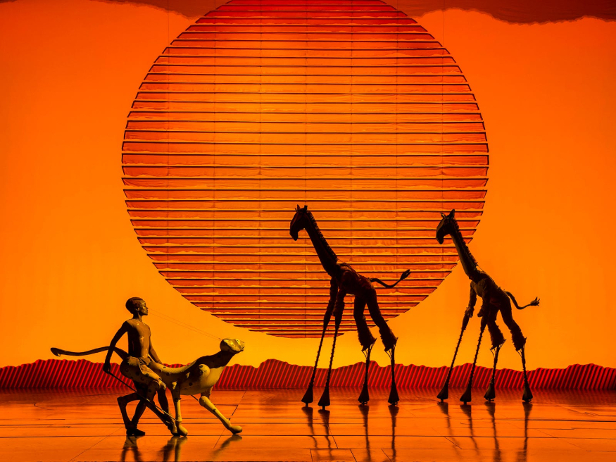 Best family/children's theatre shows in London for summer 2026: giraffe puppets silhouetted against an orange sunset in the Lion King musical
