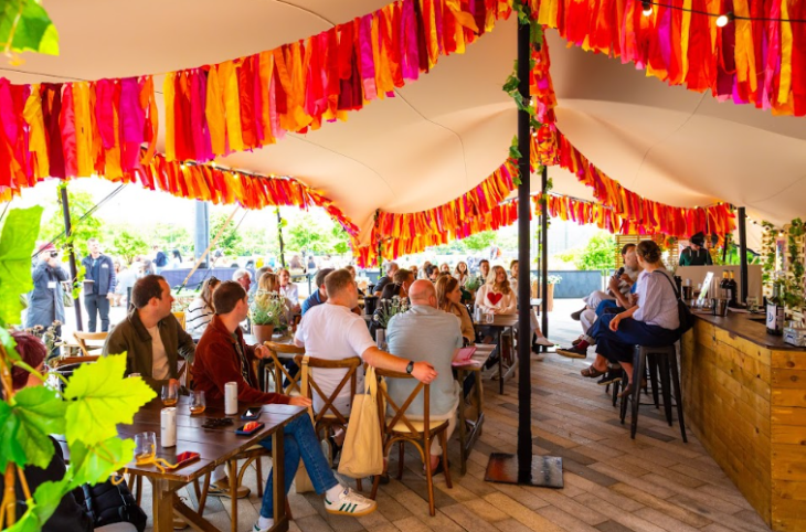 What's on in London in June 2026: people sitting in a marquee bar, decorated with colourful bunting and tassles