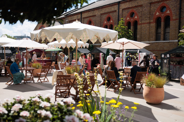 Top bank holiday weekend events London: people sitting on a patio at tables beneath sun umbrellas
