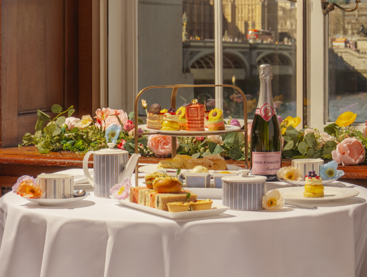 Top events in London today: a table set up for afternoon tea, with food on a tiered stand alongside a bottle of champagne and decorative flowers. 