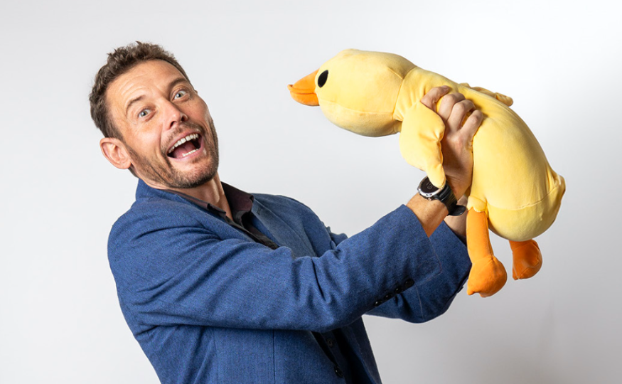 Things to do in London this weekend: a man in a blue blazer holding a yellow cuddly toy duck up