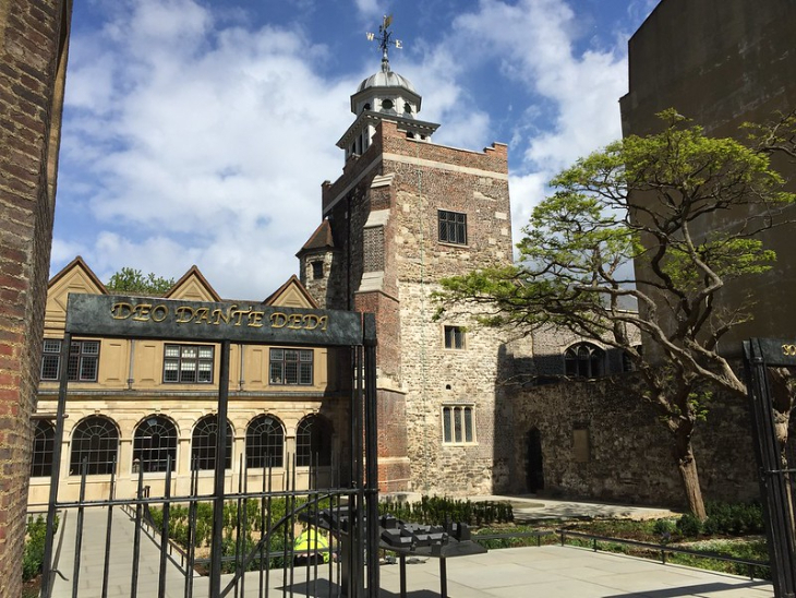 Top events in London today: A stone courtyard with a gated entrance featuring the Latin inscription "DEO DANTE DEDI," leading toward a historic brick and stone tower topped with a white cupola and weather vane.