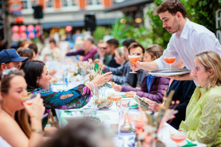 Things to do today in London: a waiter serving drinks to people at a long table