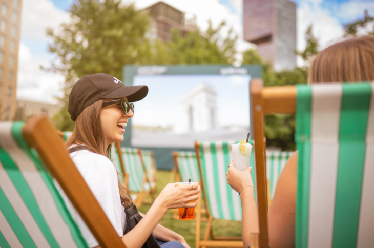Free screenings of Wimbledon 2026 matches in London: two people sitting in deckchairs with cocktails in their hands and a large screen in the background