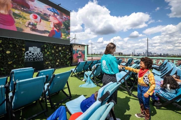 Things to do in London in the summer holidays 2026: a child dressed as Woody from Toy Story talking to a member of staff at at open air cinema