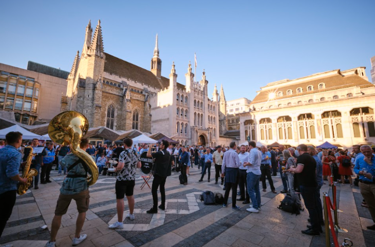 Things to do in London in July 2026: a brass band performing and people watching in the sun in Guildhall Yard