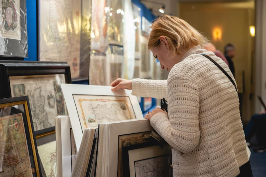 What's on in London this weekend: a woman flipping through a rack of maps at the London Map Fair