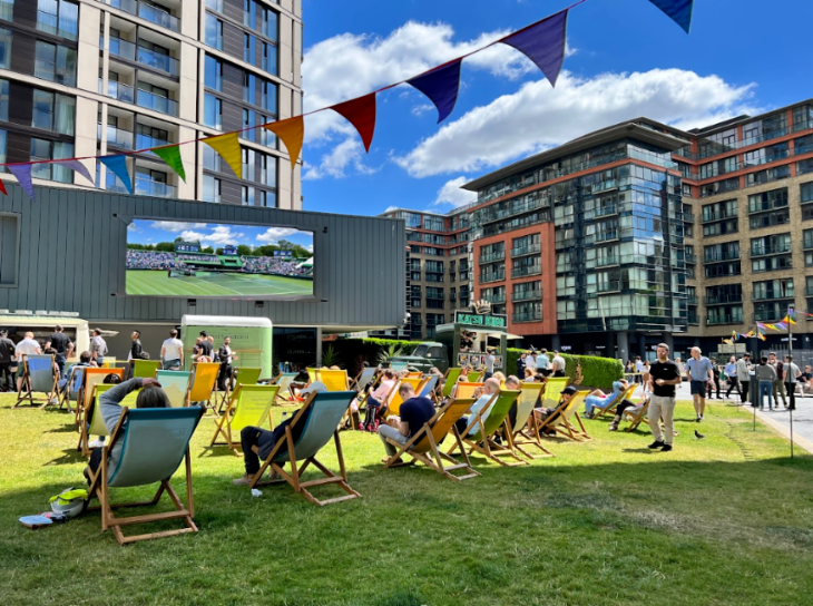 Free Wimbledon 2026 screenings London: People sitting in deckchairs on a lawn in the sun watching Wimbledon on a large screen, with colourful bunting strung overhead