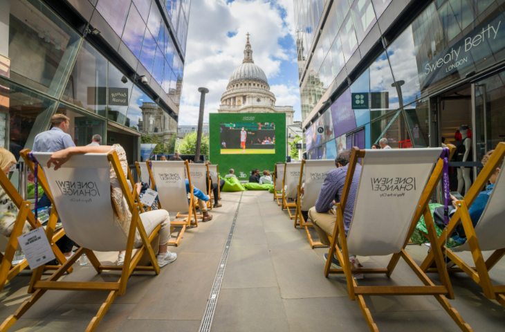 Free screenings of Wimbledon 2026 matches in London: white deckchairs facing towards a large screen showing tennis, with the dome of St Paul's Cathedral visible behind the screen
