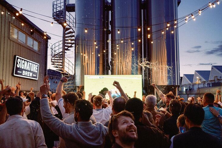People celebrating in front of a screen outside a brewery