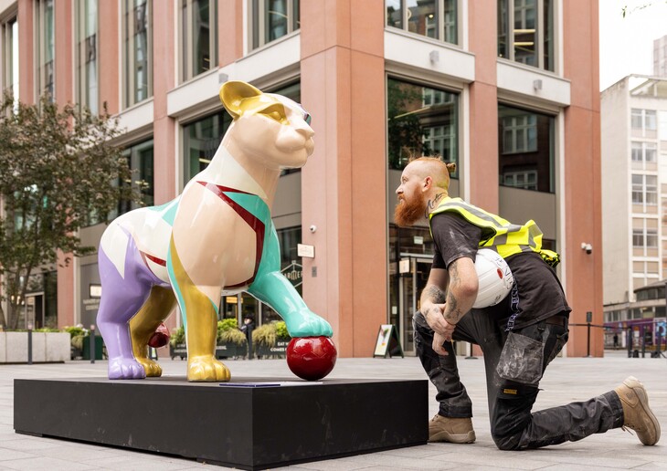 A man kneeling in front of a lioness sculpture