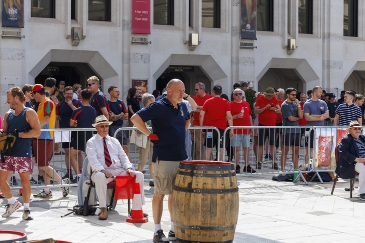A man stands with hands on hips before a barrel, possibly pondering his life choices, in Guildhall Yard