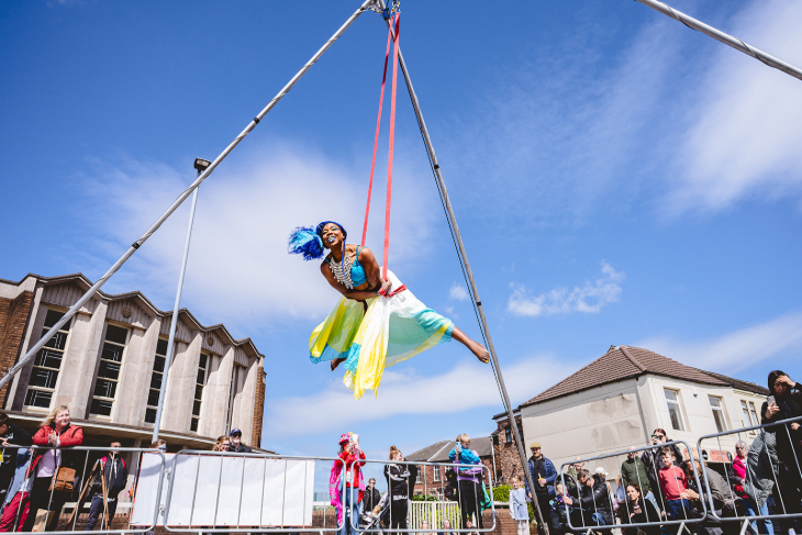 An aerial performer suspended above a street while people watch