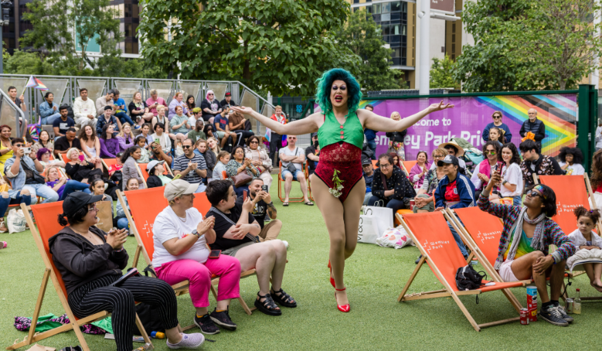 A drag performer walking among an audience sitting in deckchairs