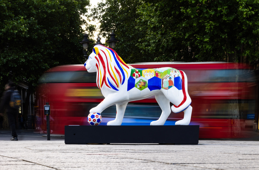 A lion with a football, and a bus driving past
