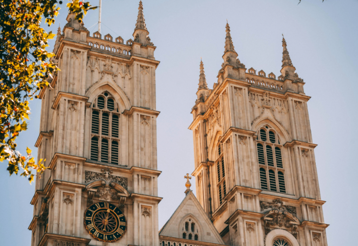 Top events in London today: A low-angle shot of the two Gothic towers of Westminster Abbey in London, framed by autumn leaves against a clear blue sky.