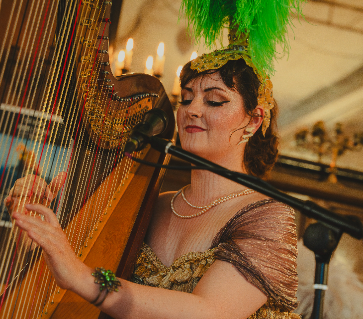 A person wearing a green feathered headdress, playing a harp