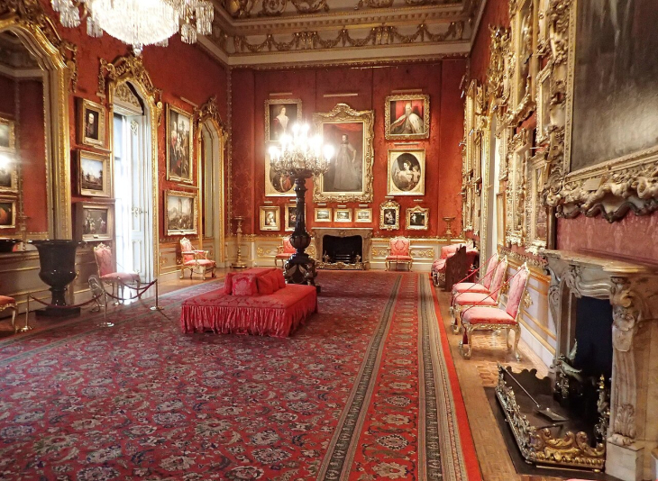 Top events in London this weekend: An opulent red drawing room with ornate gold-framed paintings, a large crystal chandelier, a red patterned carpet, and formal seating.