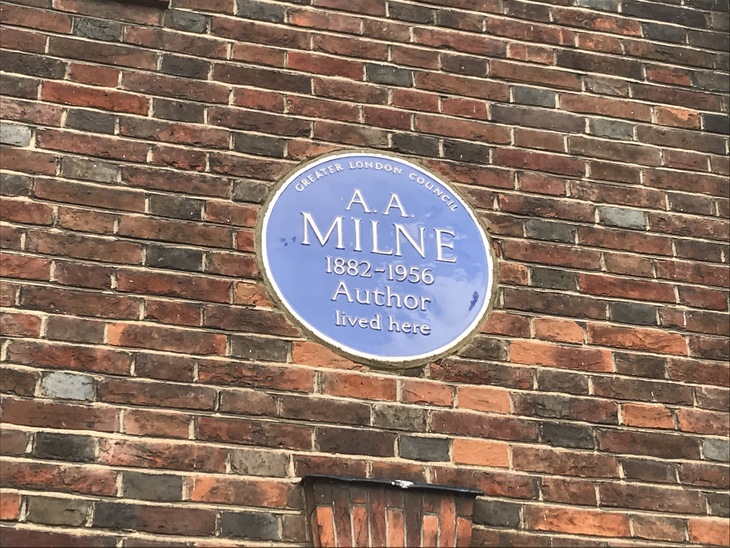 A blue circular plaque on a brick wall commemorating author A.A. Milne, who lived there from 1882 to 1956.