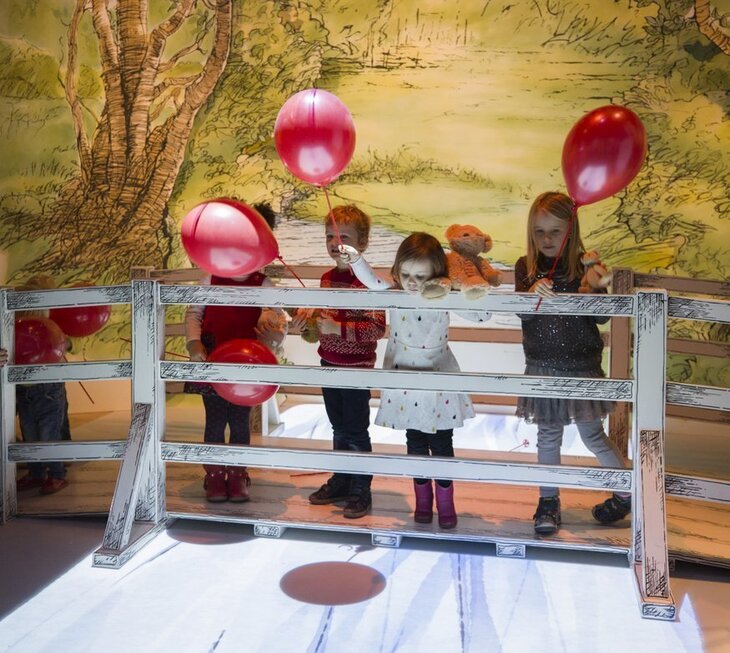 Children holding red balloons on a replica of the Pooh Sticks Bridge
