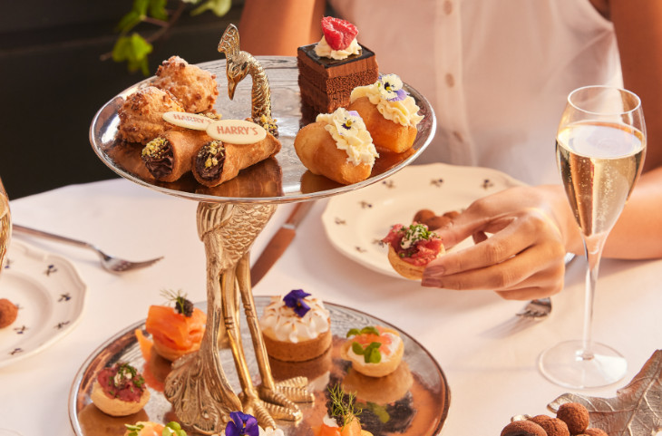 Where to have afternoon tea in London: a person's hands removing a vol-au-vent from an afternoon tea stand which is shaped like a peacock