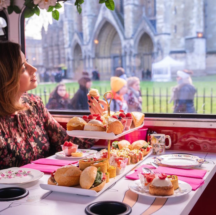 Top afternoon tea in London: a woman sitting at a table with an afternoon tea stand in front of her, looking at Westminster Abbey through a bus window.